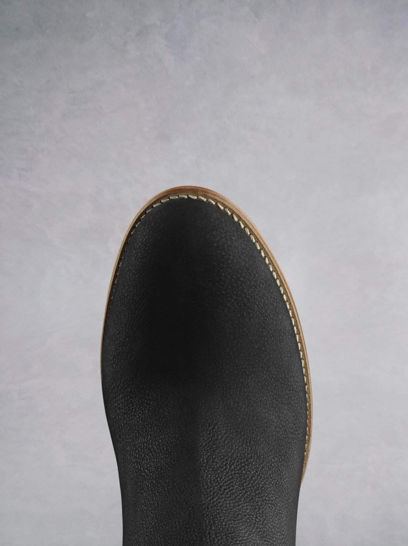 This black ankle boot has an almond toe shape highlighted by contrast white stitching. 