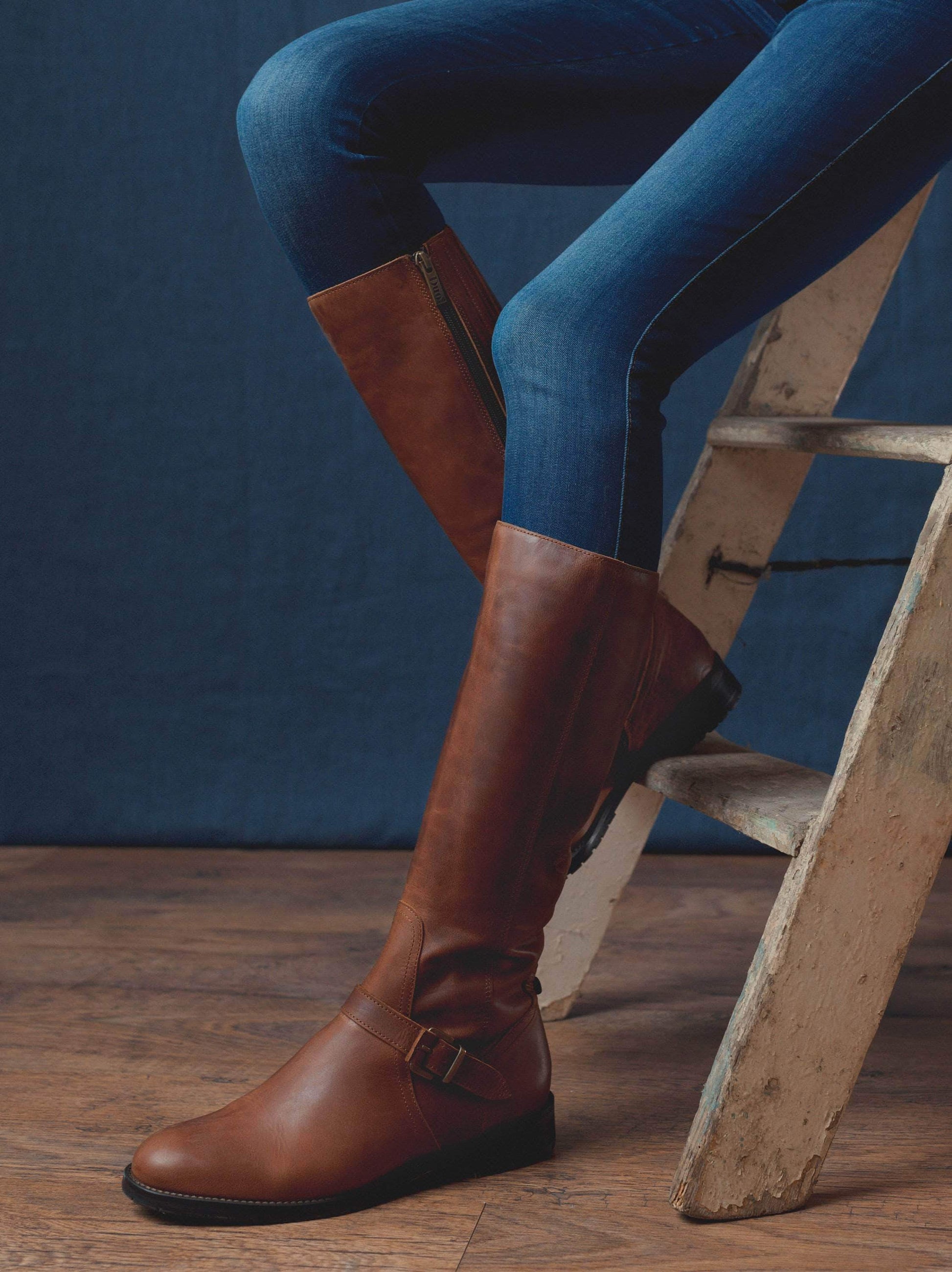 Sherwoord, a knee high boot with detailed with a brown buckled strap over the neatly cut ankle.